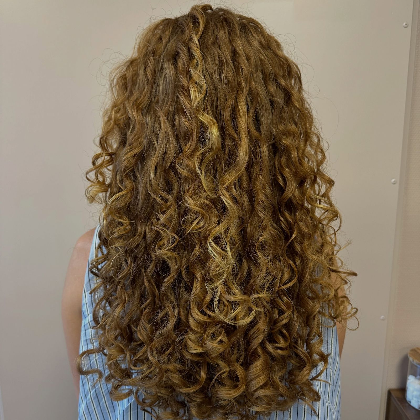 Lange, gedefinieerde goudblonde krullen van achteren, geknipt bij Kapsalon Marlies