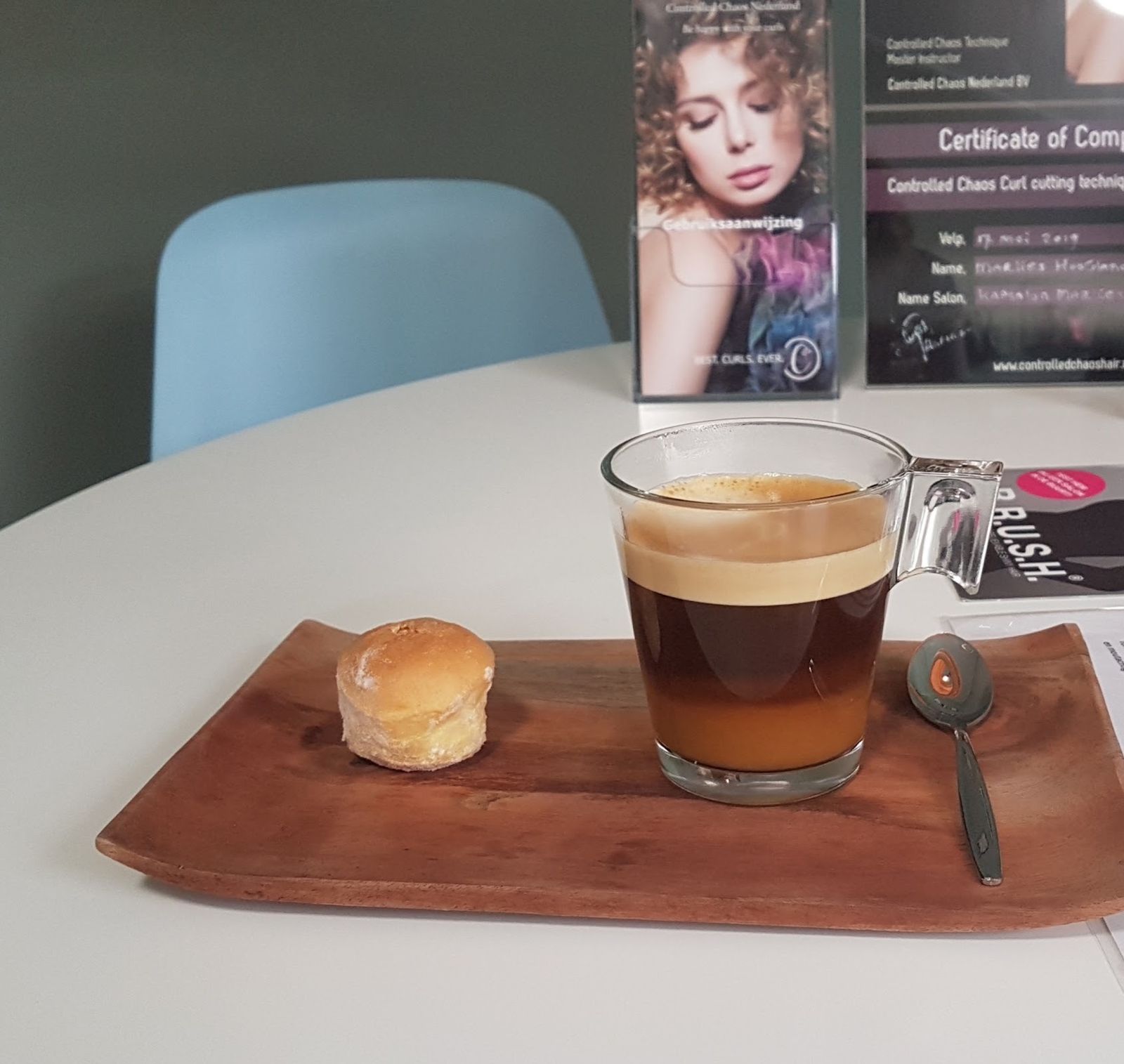 Een kop koffie met iets lekkers op een houten plankje, met het certificaat van de krullentechniek erachter