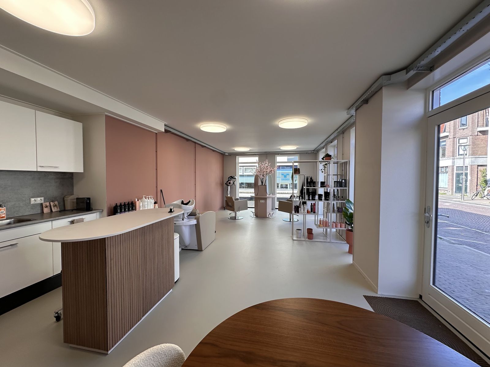 Zicht vanaf de voordeur door de salon, met de balie en de grote ramen aan de straat